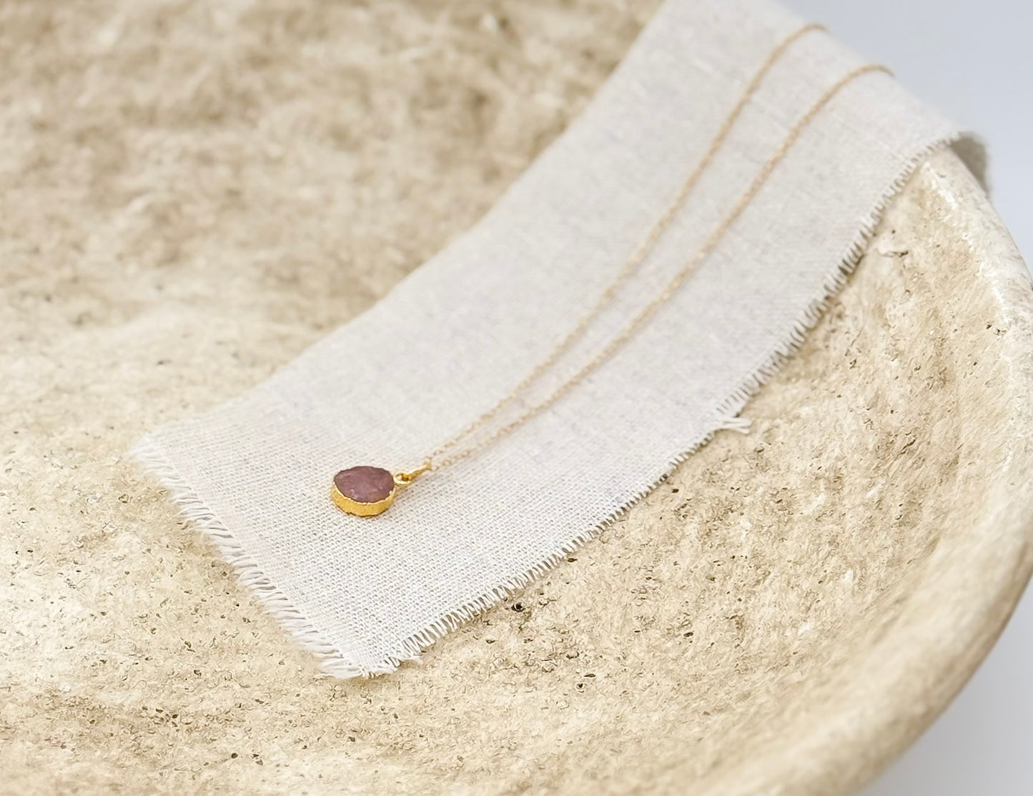 close up of the aurora necklace by studio hill designs in stone bowl on a linen strip.