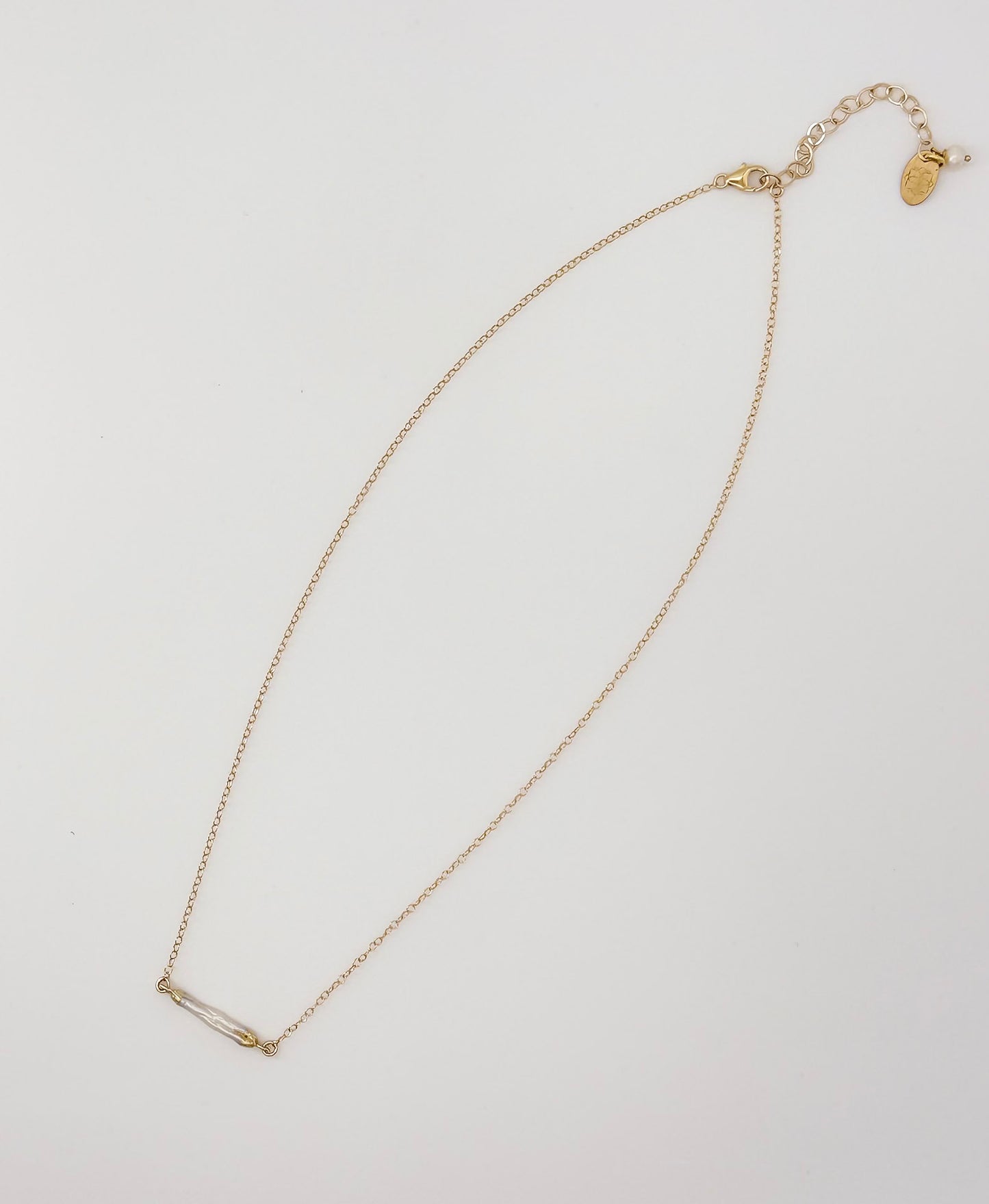 Flat lay of The Heirloom Necklace, a gold chain with pearl bar pendant, by Studio Hill Designs.