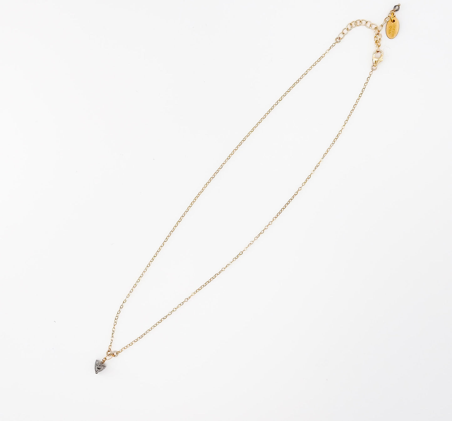 Flat lay of The Luna Necklace, a gold chain with black rutilated quartz pendant by Studio Hill Designs against a neutral background