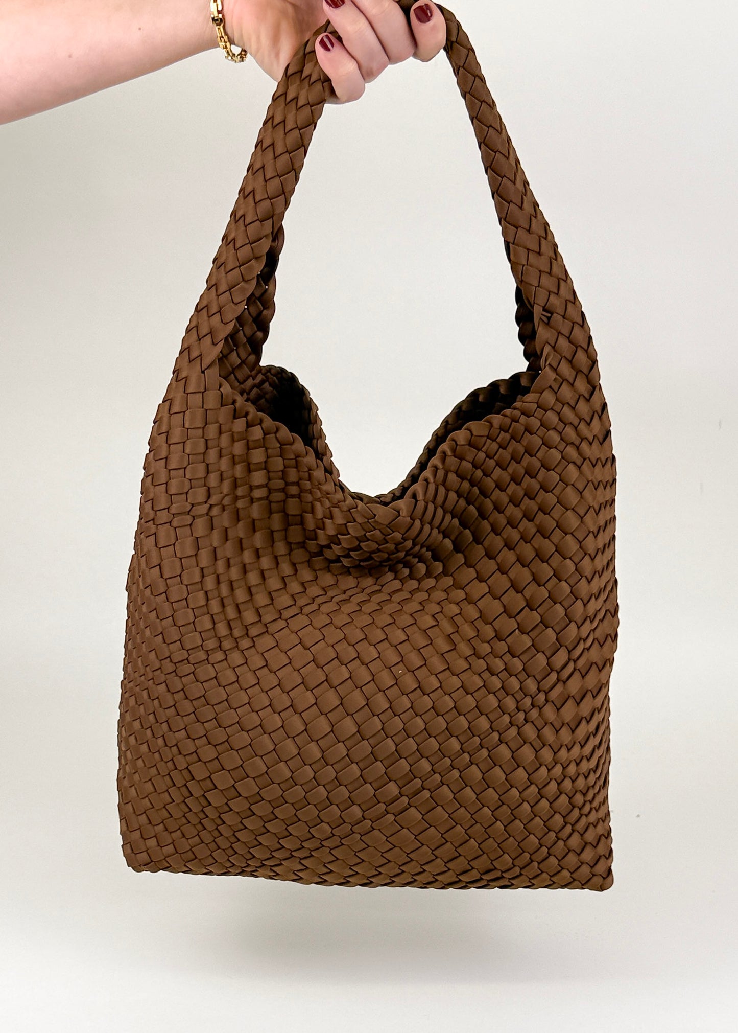 The Autumn Woven Tote handbag in brown by Studio Hill Designsheld by a person against a white background