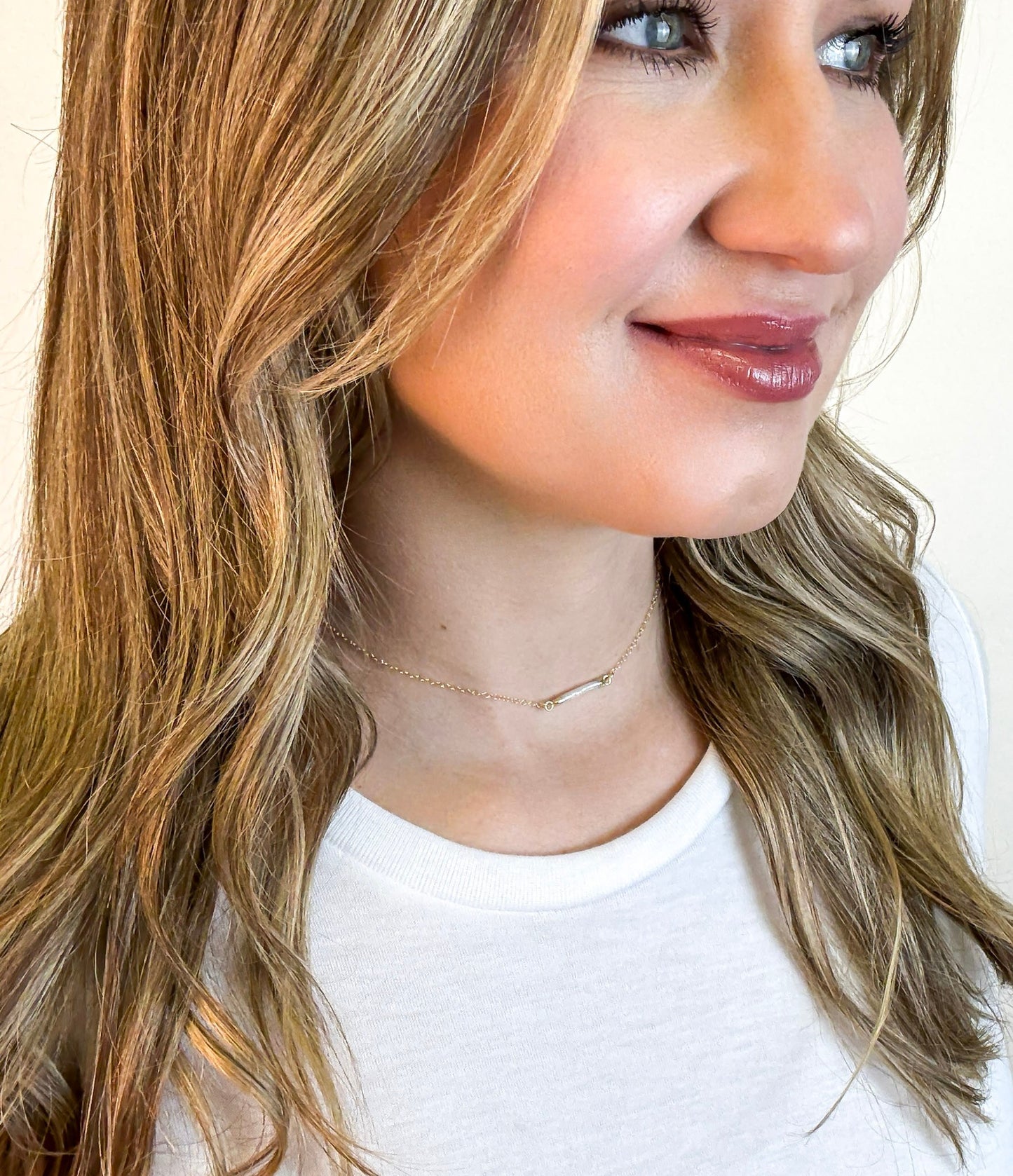 Close up of woman wearing The Heirloom Necklace, a gold necklace with a pearl bar pendant, by Studio Hill Designs.