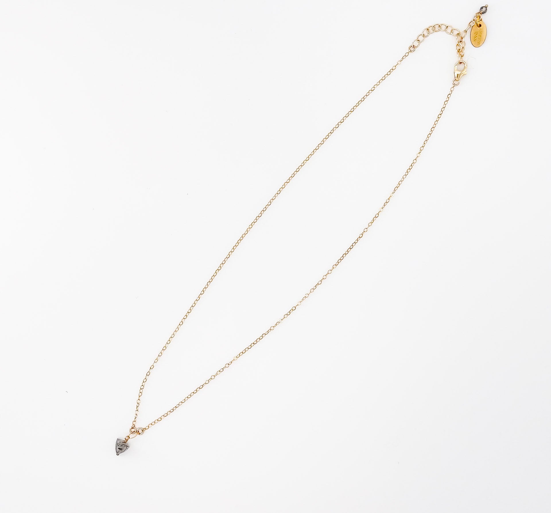 Flat lay of The Luna Necklace, a gold chain with black rutilated quartz pendant by Studio Hill Designs against a neutral background