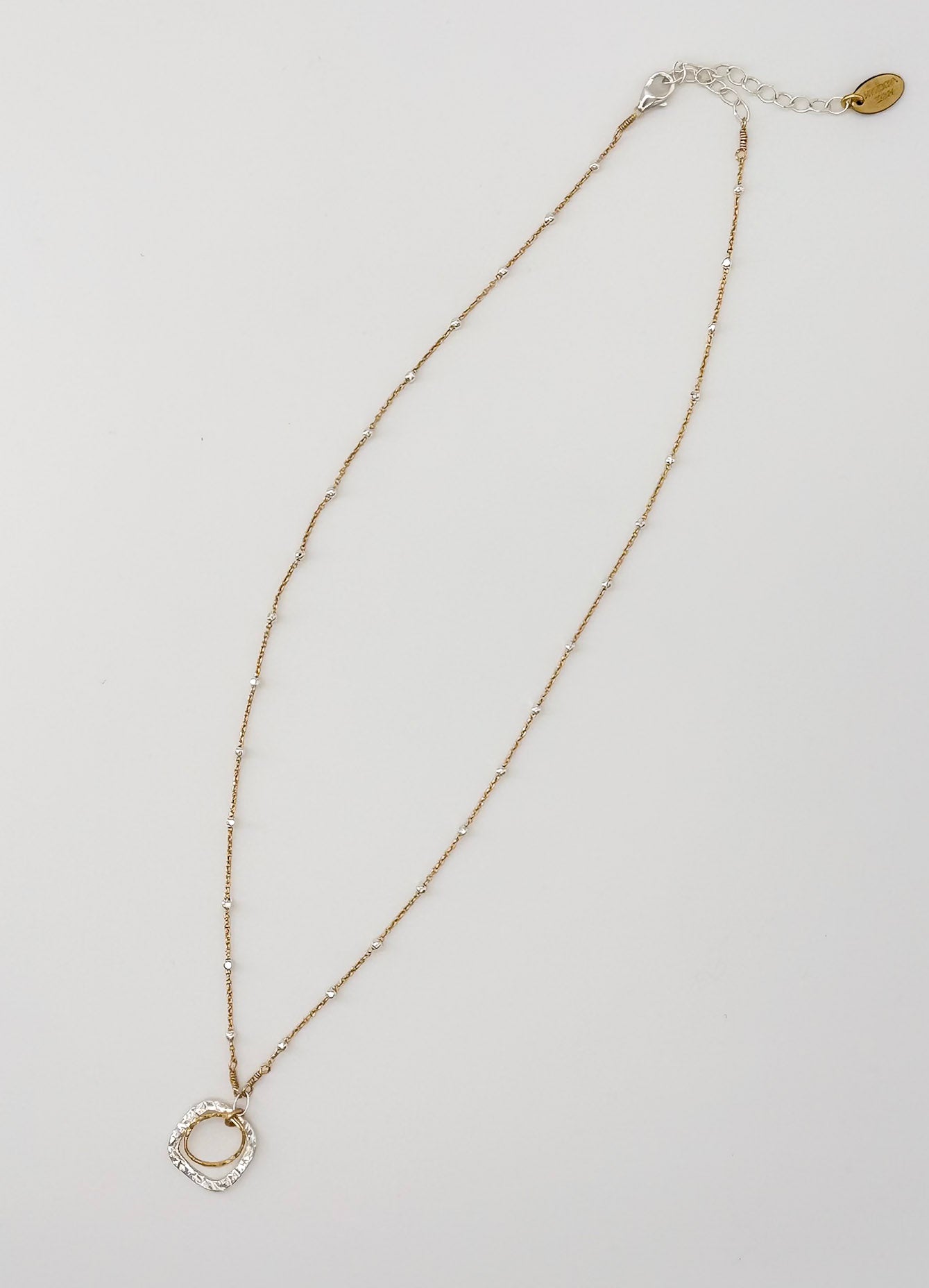 Flat lay of The Serenity Necklace, a gold and silver chain with gold and silver circular pendant, by Studio Hill Designs.