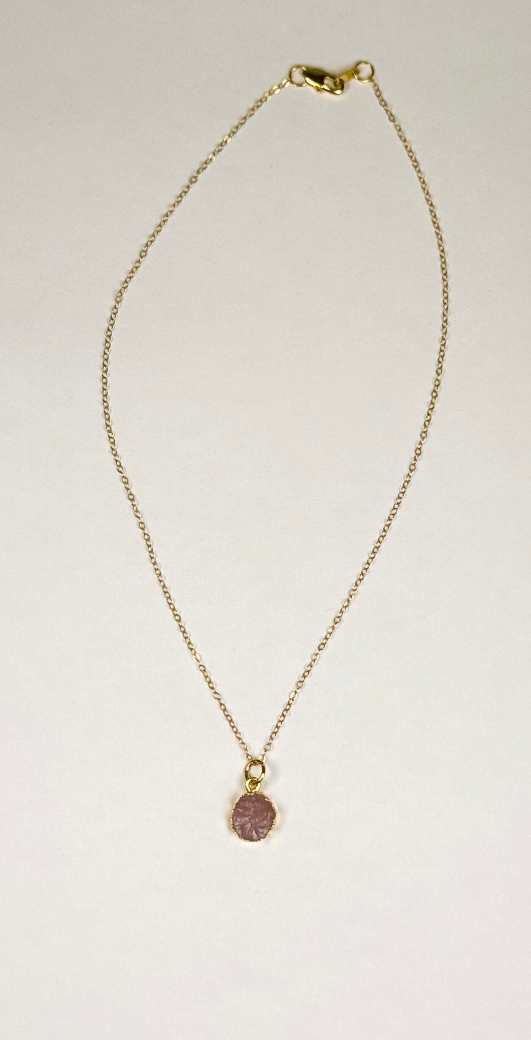 Flat lay image of The Aurora Necklace handmade by Studio Hill Designs. Gold filled chain with pink natural stone pendant