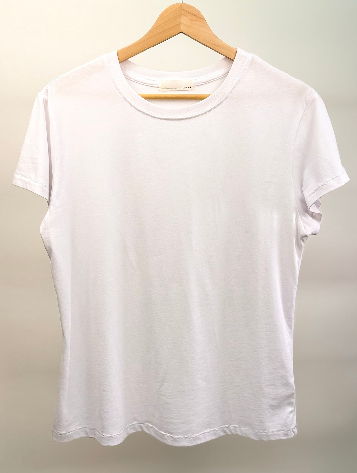 The Essential Cotton White t-shirt by Studio Hill Designs on a wooden hanger against a plain background