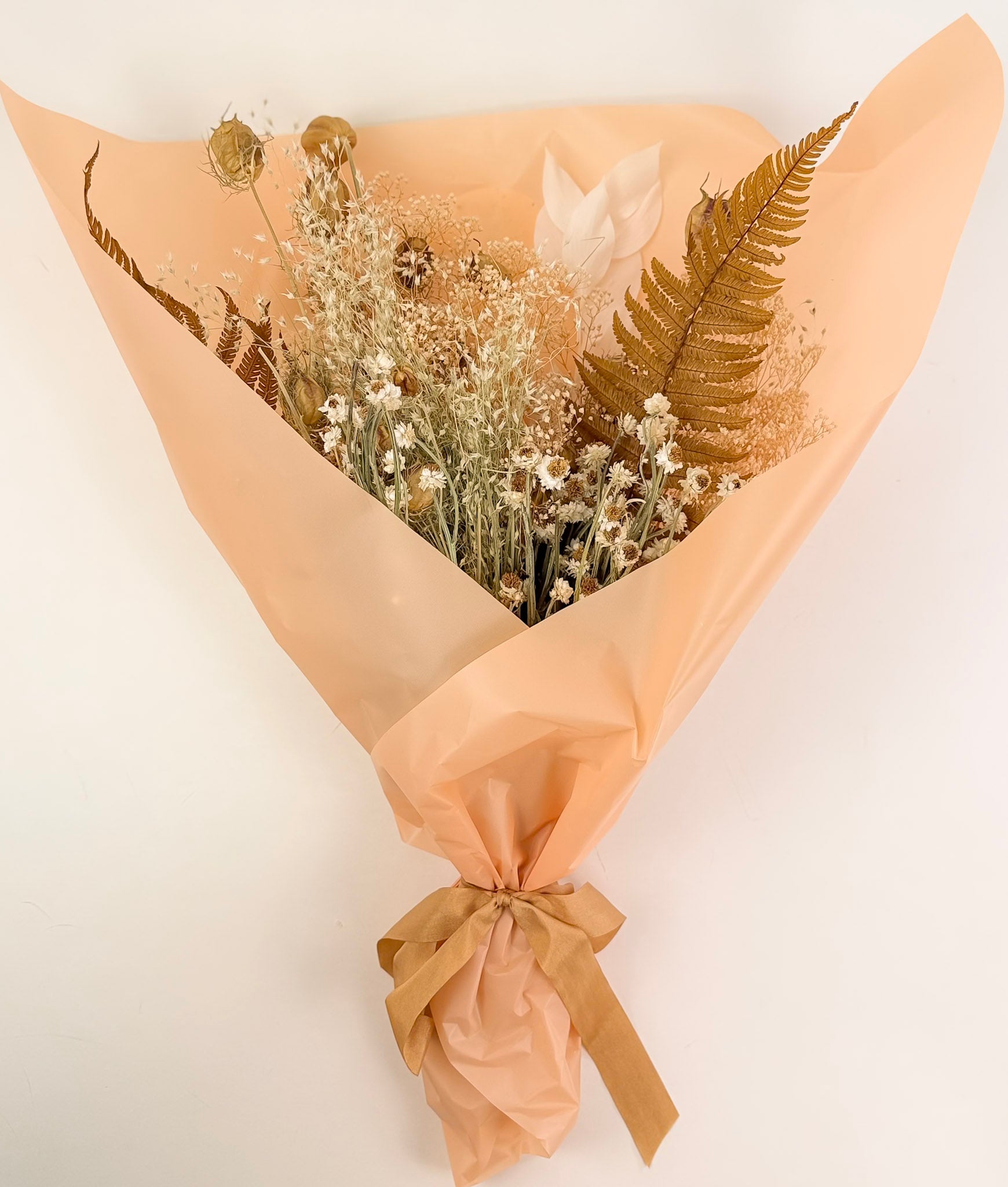 The Harvest Dried Floral Bouquet wrapped in beige paper with a ribbon on a white background by Studio Hill Designs.