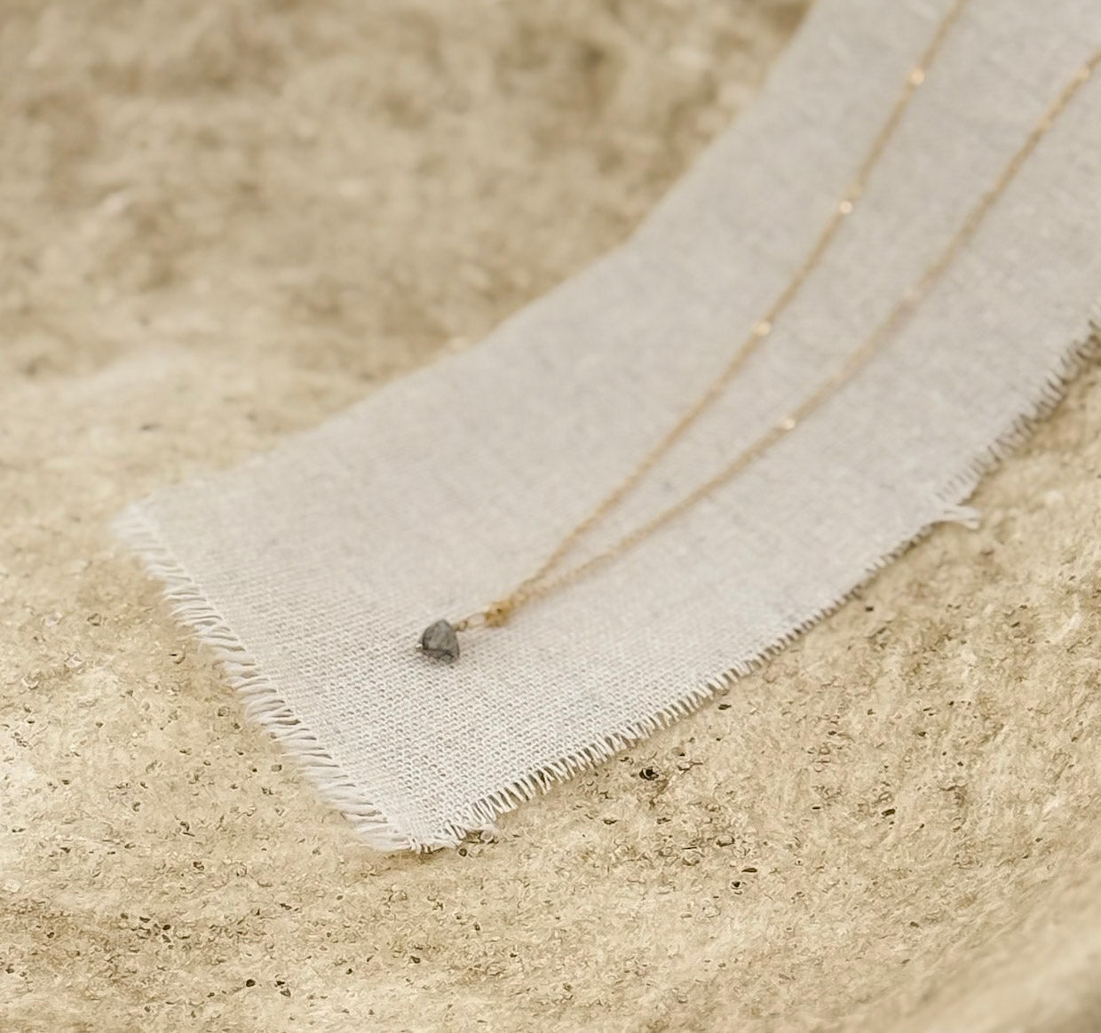 The Luna Necklace, a gold chain with black rutilated quartz pendant by Studio Hill Designs styled in a stone bowl on a linen strip.