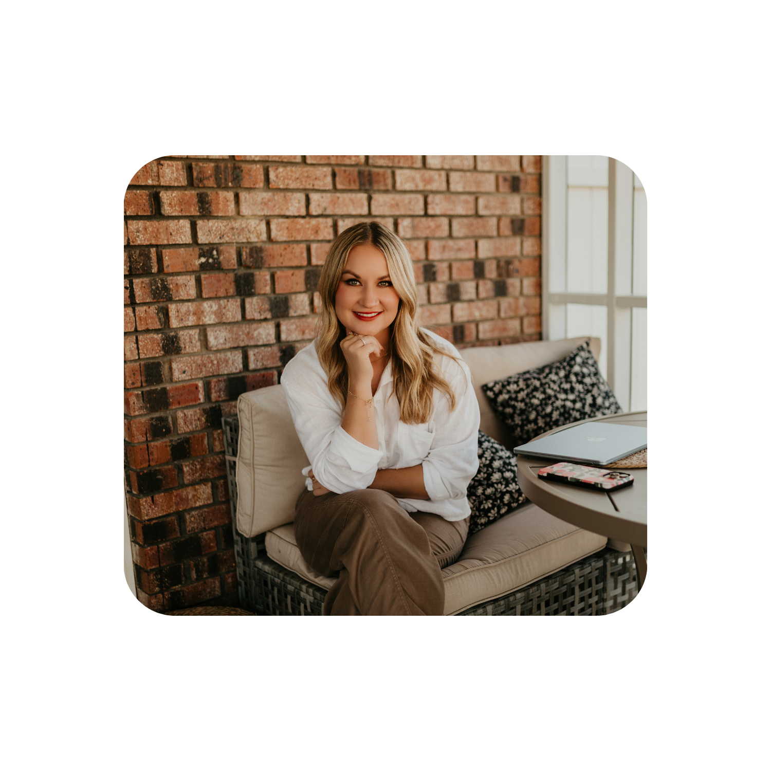 Studio Hill Designs owner sitting on a couch smiling in a cozy room with a brick wall.
