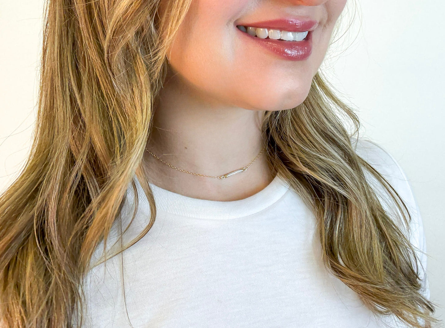 Close up of woman wearing The Heirloom Necklace, a gold necklace with a pearl bar pendant, by Studio Hill Designs.