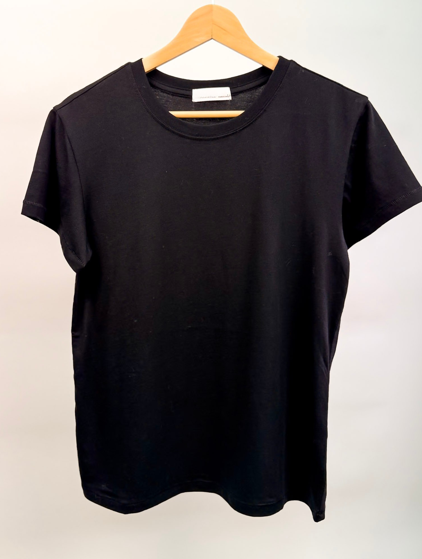 The Essential Cotton Black  t-shirt by Studio Hill Designs on a wooden hanger against a plain background