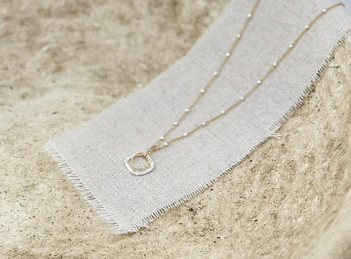 The Serenity Necklace styled in a stone bowl on a linen strip by Studio Hill Designs.