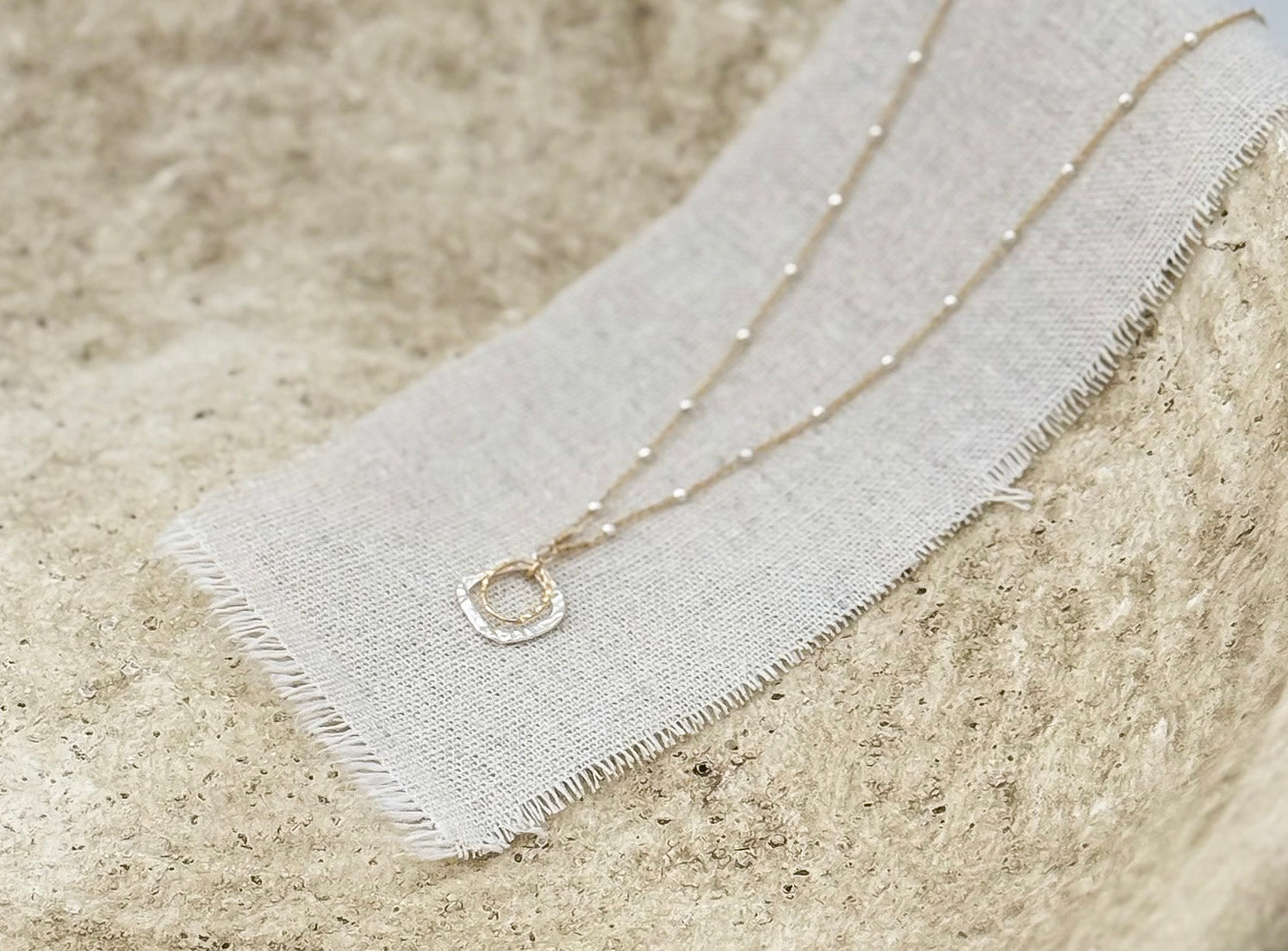 The Serenity Necklace styled in a stone bowl on a linen strip by Studio Hill Designs.