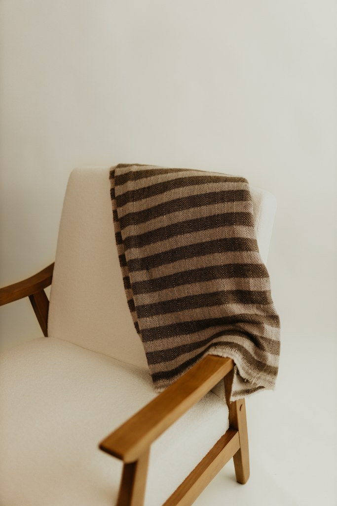 Beige chair with the Hamilton Cashmere Throw, a striped brown and beige blanket, draped over it against a white background by Studio Hill Designs.